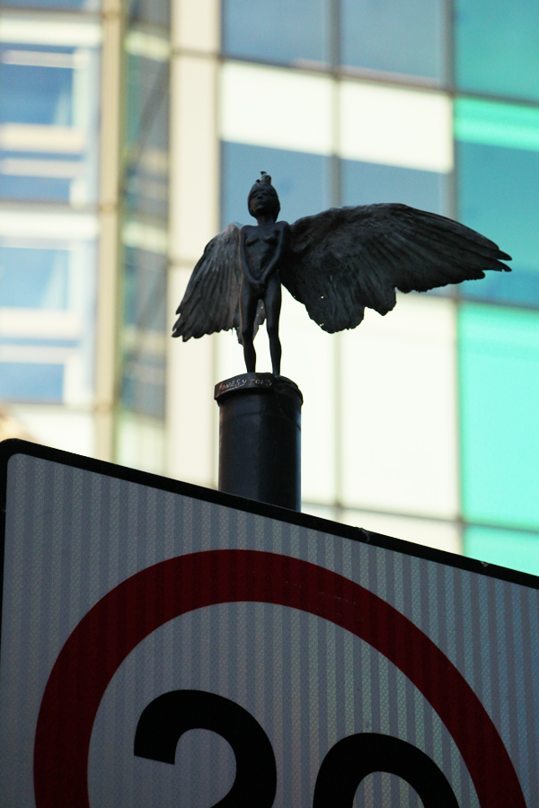 Streetart in London, Figur mit Flügeln auf einem Straßenschild