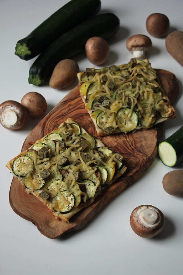 Vegane Blätterteig-Tarte auf Holzbrett mit frischem Gemüse dekoriert