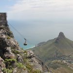Aussicht vom Tafelberg auf den Lionshead. Davor fährt eine Seilbahngondel den Berg hinauf.