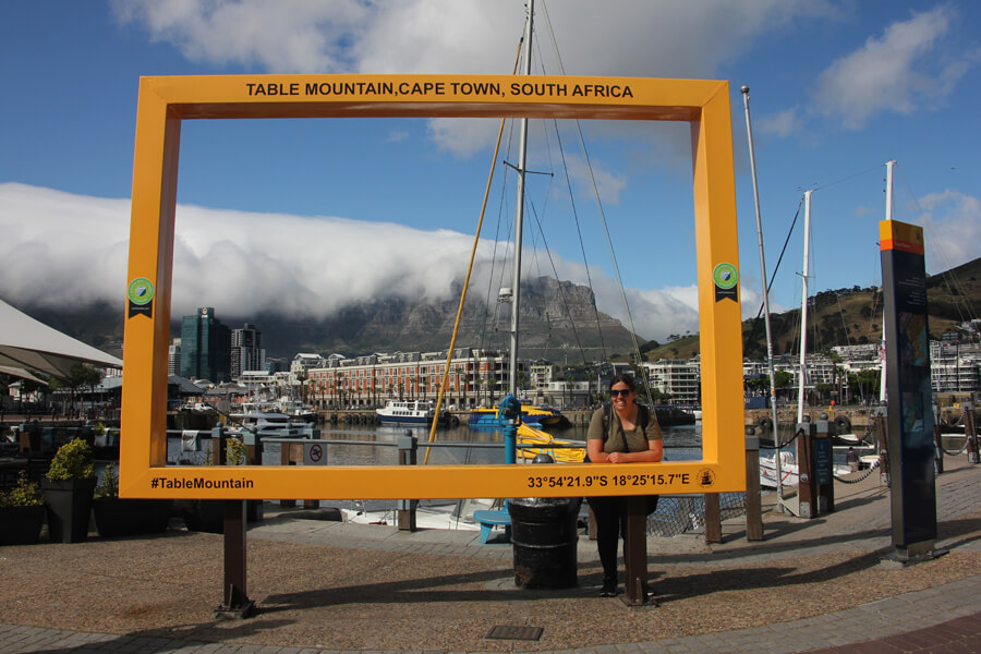 Ich in einem gelben Bilderrahmen-Fotospot an der Waterfront mit dem Tafelberg im Hintergrund.