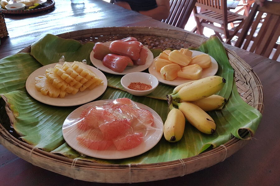 Verschiedene exotische Obstsorten werden auf einem geflochtenen Tablett und einem Bananenblatt serviert.