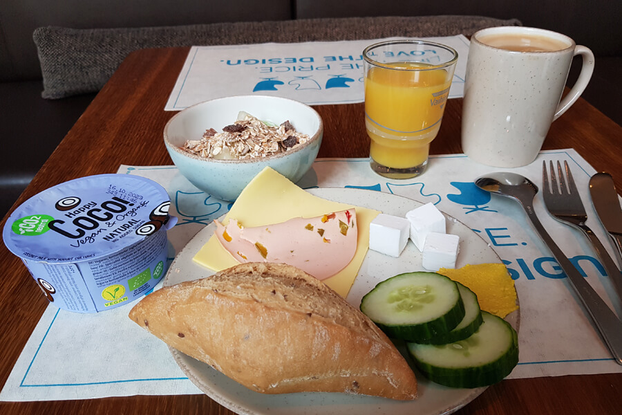 Meine vegane Frühstücksauswahl im Motel One Leipzig: Brötchen mit veganem Käse und Wurstaufschnitt, Kokosjoghurt, Müsli, Kaffee und Orangensaft.
