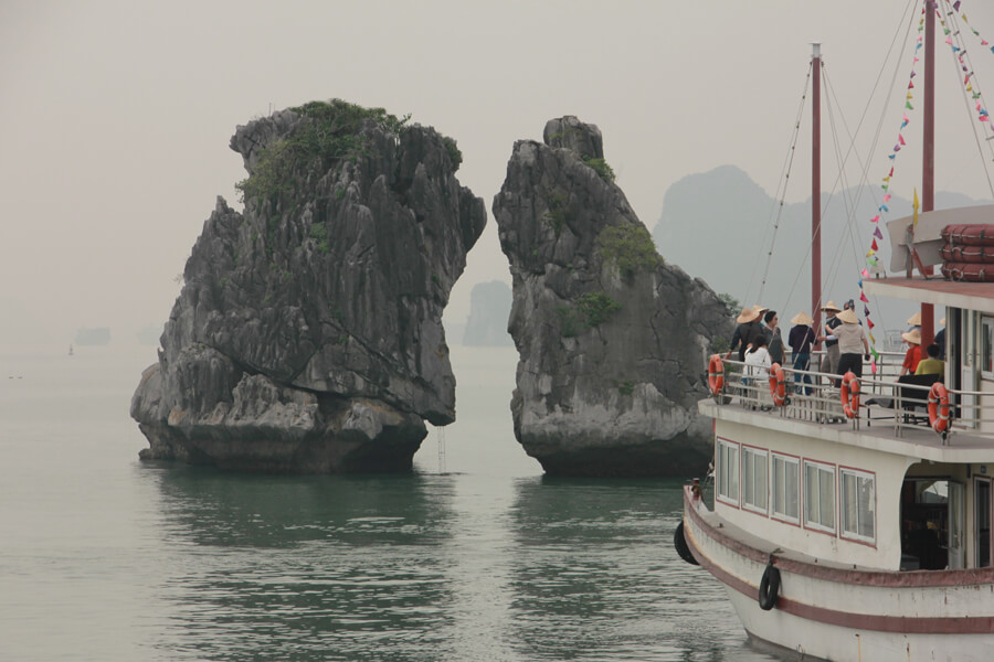 Touristenboot fährt vor einem Felsen in der Halong Bucht.