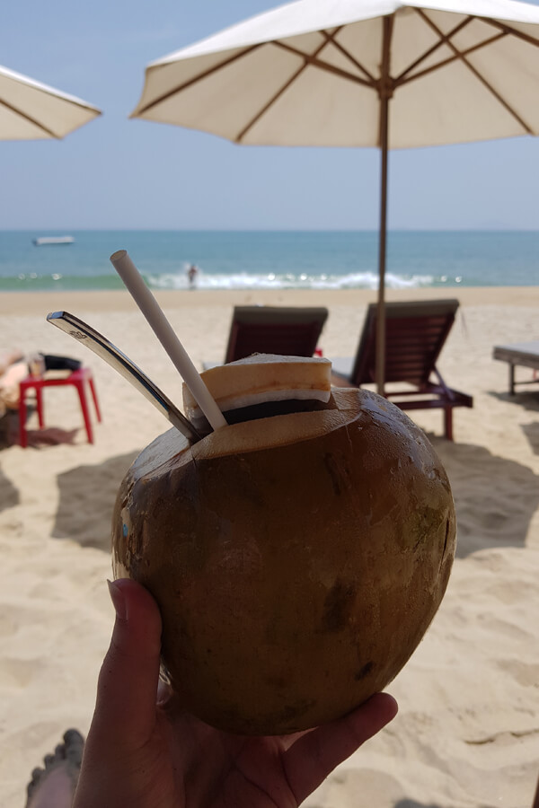 Am Strand von An Band mit einer frischen Kokosnuss in der Hand und Blick aufs Meer.