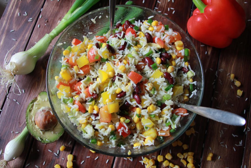 Eine Schüssel veganer Reissalat mit buntem Gemüse.