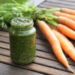 Ein Glas Möhrengrün-Pesto vor einem Bund Möhren