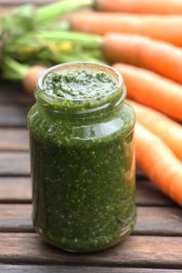Ein Glas Möhrengrün-Pesto vor einem Bund Möhren