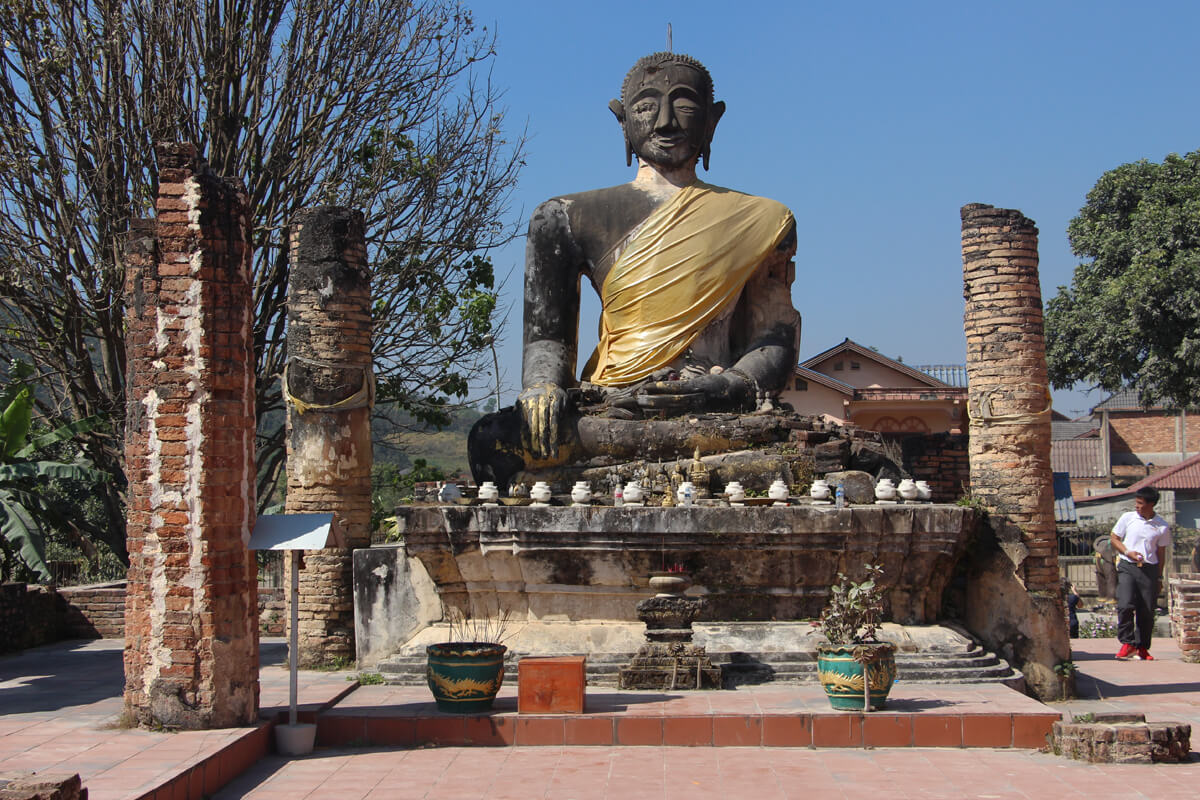 Durch Bomben teilweise zerstörte Buddha Figur in einer Tempelruine in Phonsavan