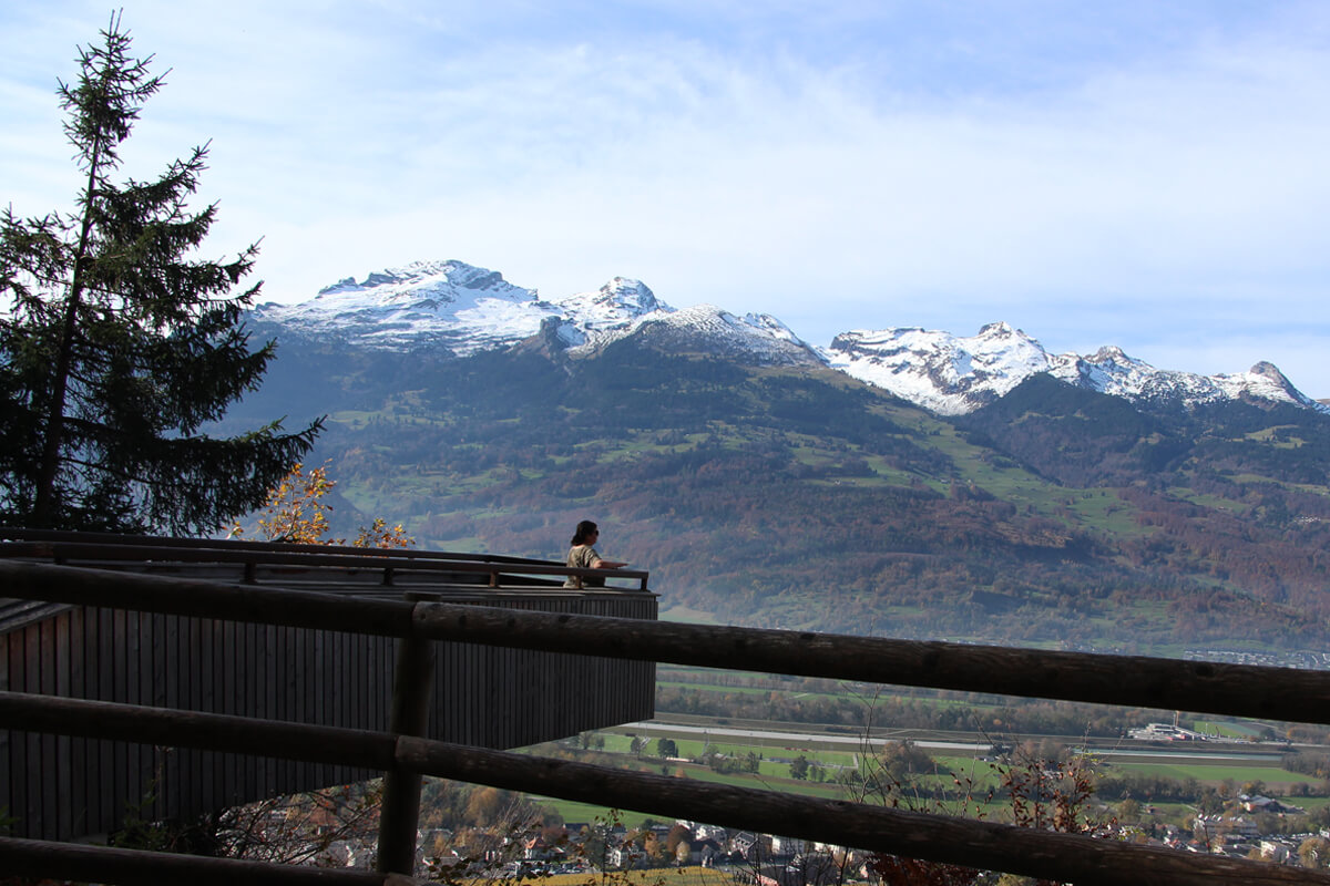 Ich auf einem Panorama Skywalk in Liechtenstein vor schneebedeckten Berggipfeln