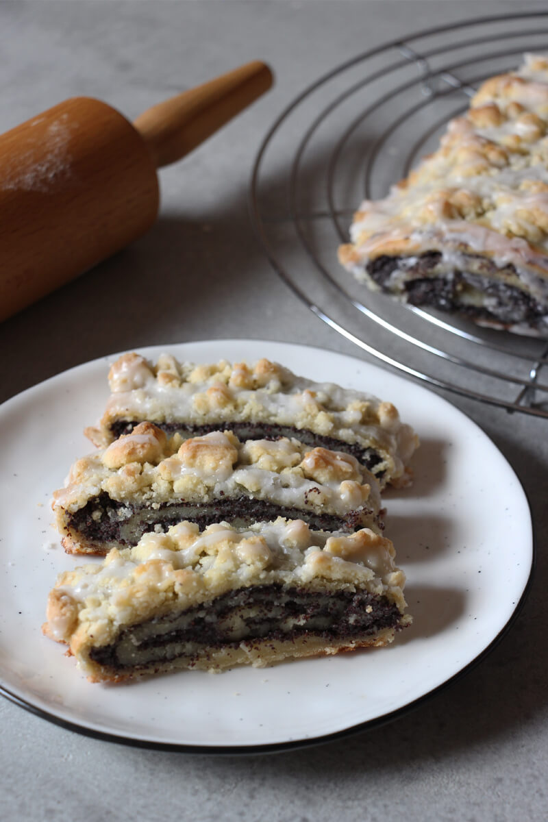 drei Stücke veganer Mohnstriezel auf einem Teller, daneben ein Nudelholz
