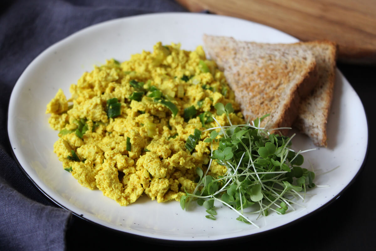 Ein Teller mit Scrambled Tofu, Toast und grünen Sprossen.