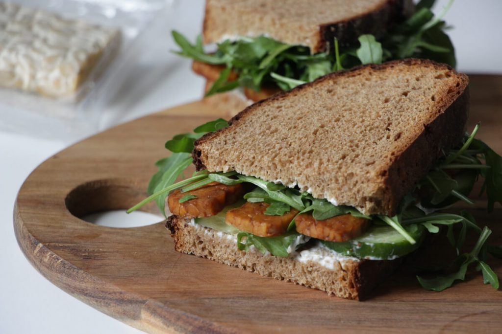 Sandwich mit Tempeh und Rucola auf einem Holzbrett