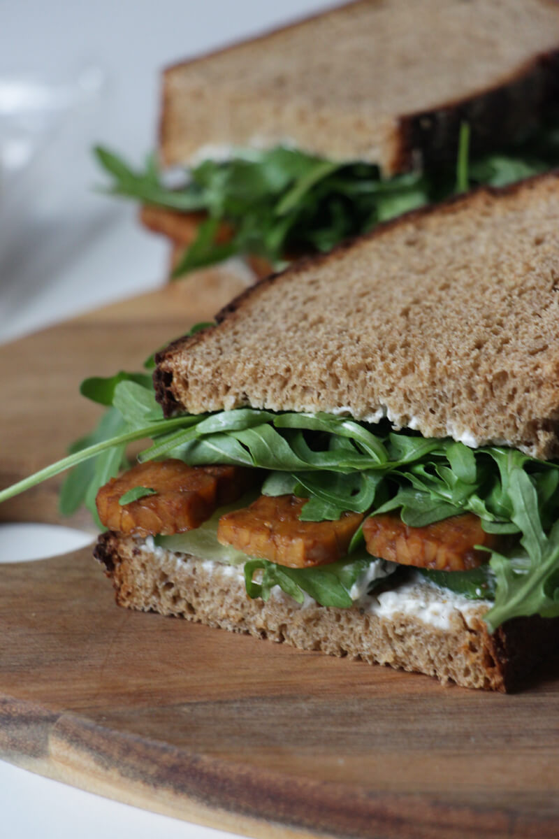 Sandwich mit Tempeh und Rucola auf einem Holzbrett