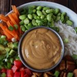 vegane Reisnudelbowl mit frischem Gemüse, angebratenem Tempeh und einer Schale mit Erdnussoße in der Mitte