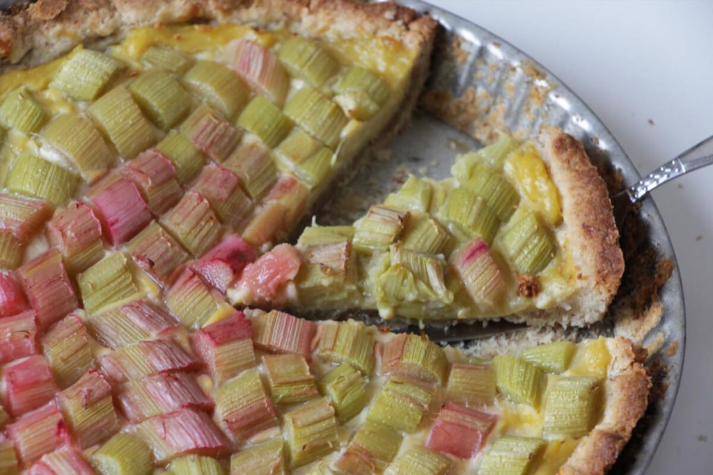 Vegane Rhabartertarte in einer Form mit einem herausgeschnittenen Stück auf einem Tortenheber.