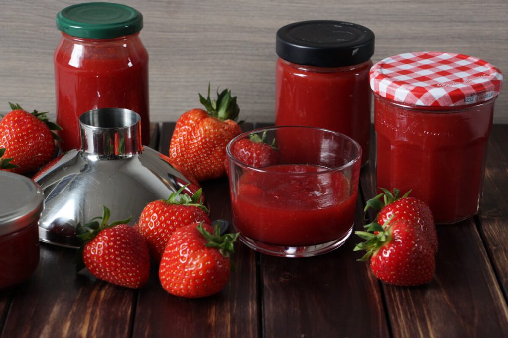 verschiedene Gläser mit frisch gekochter Erdbeermarmelade und ein paar frische Erdbeeren