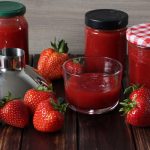 verschiedene Gläser mit frisch gekochter Erdbeermarmelade und ein paar frische Erdbeeren