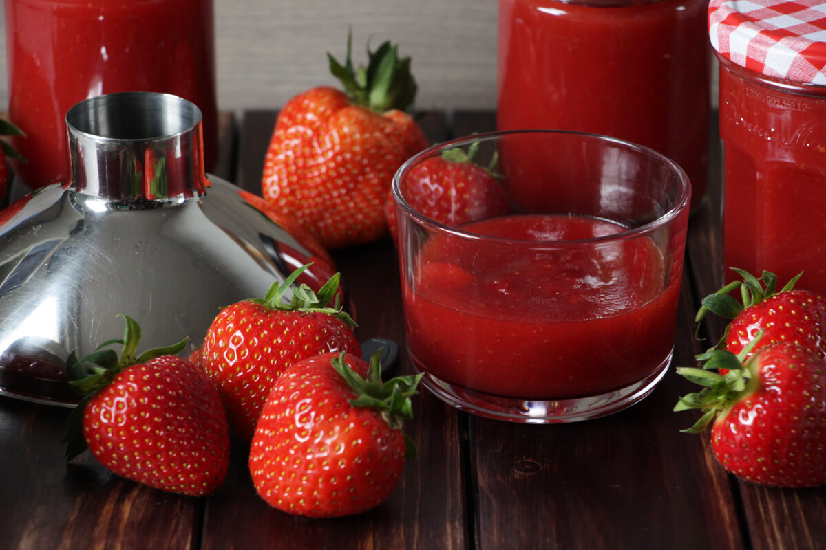 verschiedene Gläser mit frisch gekochter Erdbeermarmelade und ein paar frische Erdbeeren