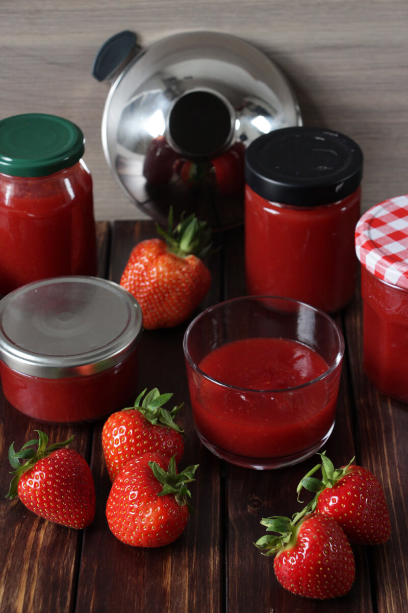 verschiedene Gläser mit frisch gekochter Erdbeermarmelade und ein paar frische Erdbeeren