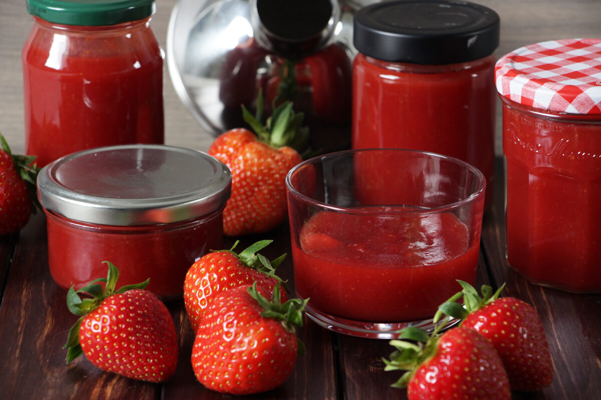 verschiedene Gläser mit frisch gekochter Erdbeermarmelade und ein paar frische Erdbeeren