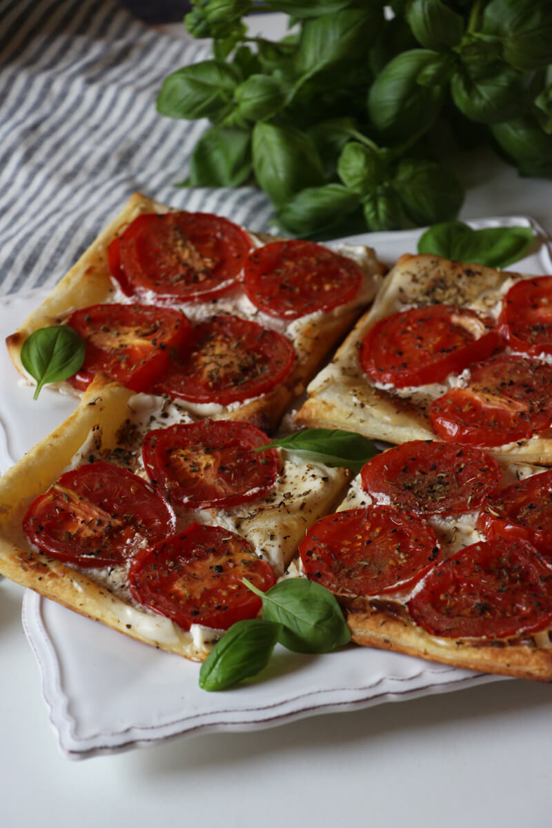 vegane Tomaten-Blätterteig-Tartes auf einem Teller mit Basilikum angerichtet