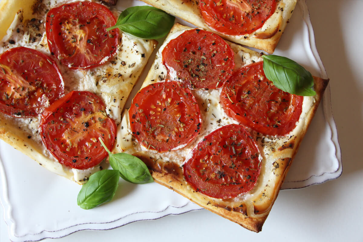 vegane Tomaten-Blätterteig-Tartes auf einem Teller mit Basilikum angerichtet