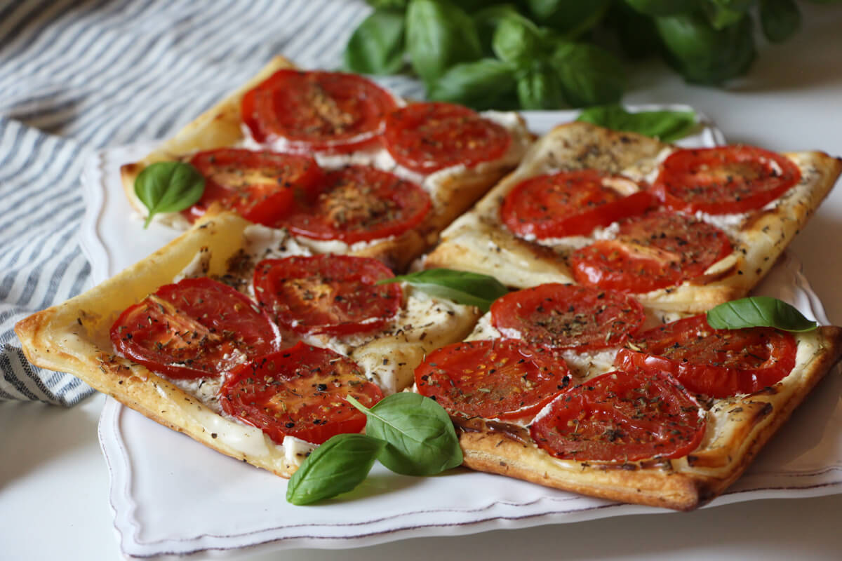 vegane Tomaten-Blätterteig-Tartes auf einem Teller mit Basilikum angerichtet