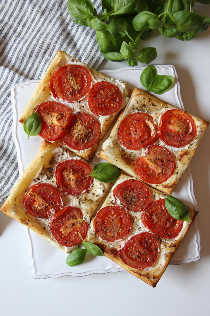 vegane Tomaten-Blätterteig-Tartes auf einem Teller mit Basilikum angerichtet