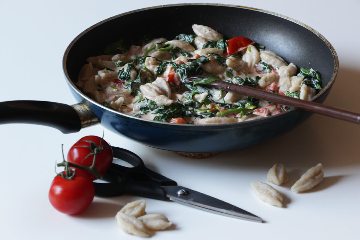 vegane Scherenpasta mit Soße in einer Pfanne, daneben eine Küchenschere und lose Pasta