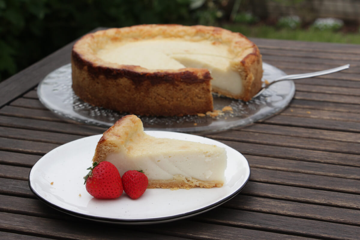 Angeschnittener veganer Käsekuchen auf einer Platte mit einem Stück auf einem Teller davor