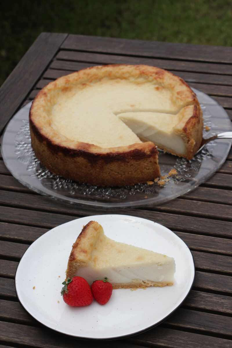 Angeschnittener veganer Käsekuchen auf einer Platte mit einem Stück auf einem Teller davor