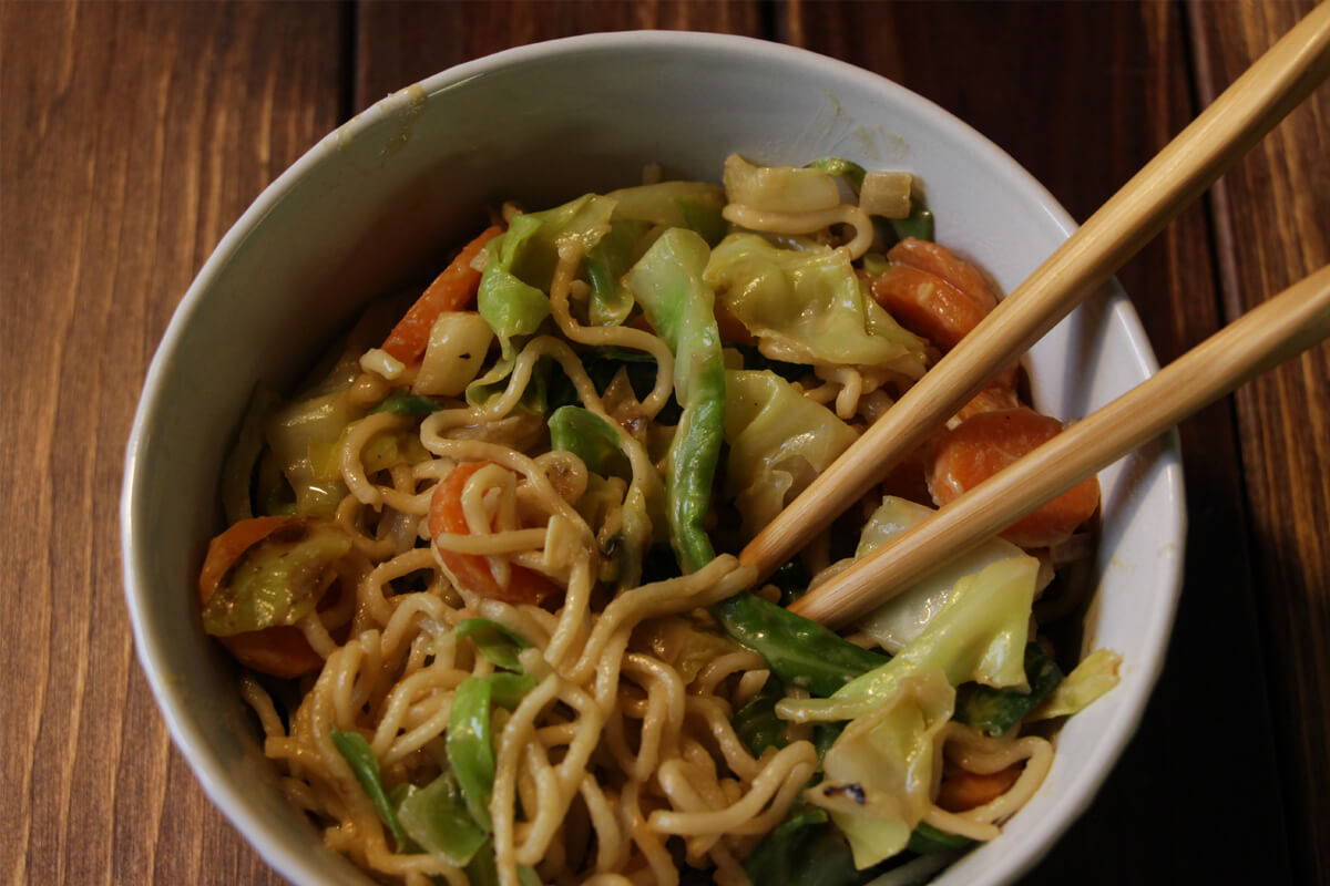 vegane Mie-Nudel-Wok-Pfanne mit Möhren und Spitzkohl in einem Schälchen mit Stäbchen
