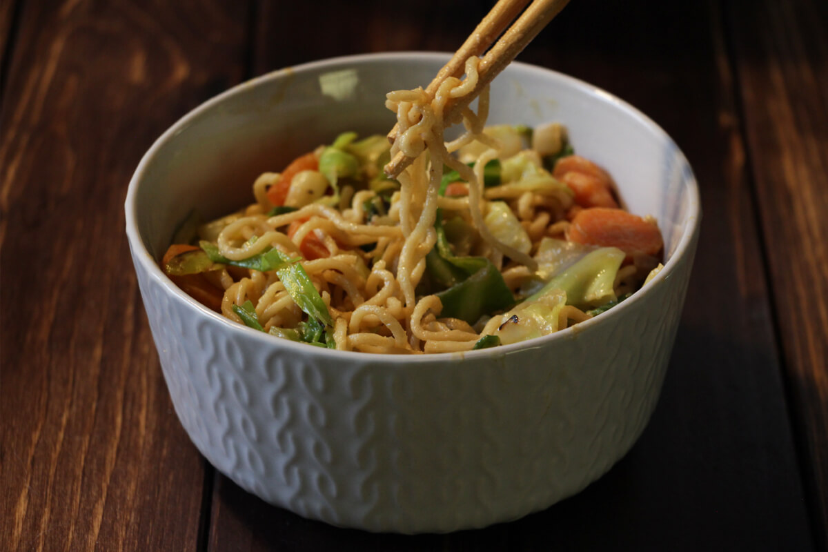 vegane Mie-Nudel-Wok-Pfanne mit Möhren und Spitzkohl in einem Schälchen mit Stäbchen